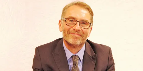 Headshot of man in grey suit jacket with purple tie and glasses