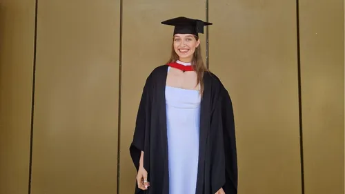 A girl wearing a black cap and gown over a white dress smile for a picture