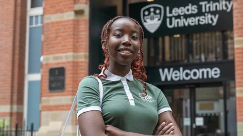 A female student wearing a green top smiling outside the Leeds Trinity University City Campus.