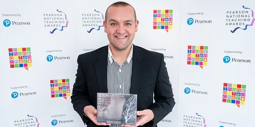 A white man in his 20s smiling and holding a Pearson National Teaching Award.