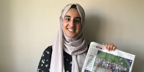 Female student in grey headscarf holding newspaper