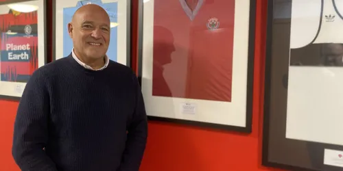 Older man stands in front of framed shirt on wall