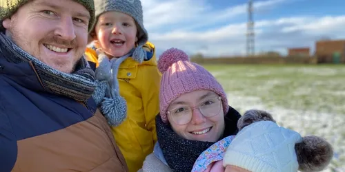 Woman in pink bobble hat, glasses, black scarf with two children and husband