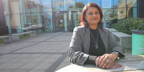 Female lecturer sat on bench in front of university building