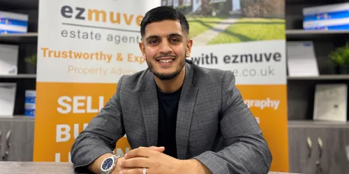 Male sits at desk smiling in front of Ezmuve sign