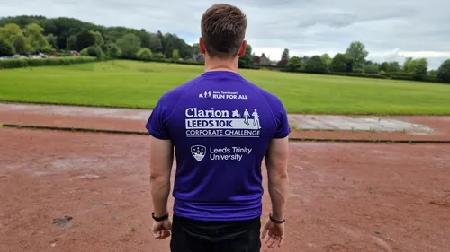 A man with dark hair wearing a purple tee shirt stands on a running track