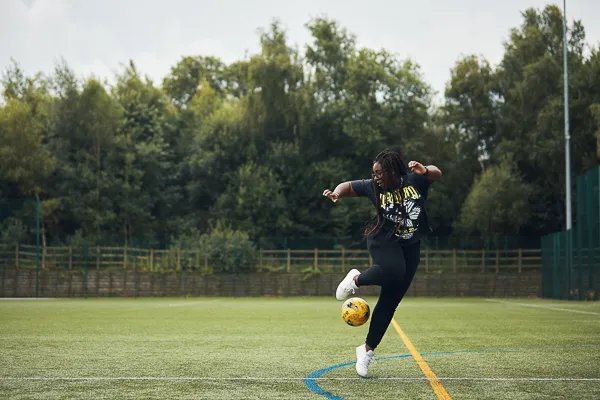 Female student performing a trick with a football on a 3G pitch.