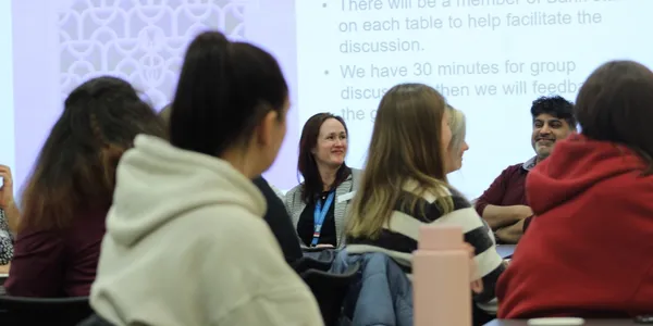 Students facing a screen with a woman and man visible on the panel