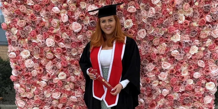 Girl with red hair in a graduation gown stands with scroll against flower drop background