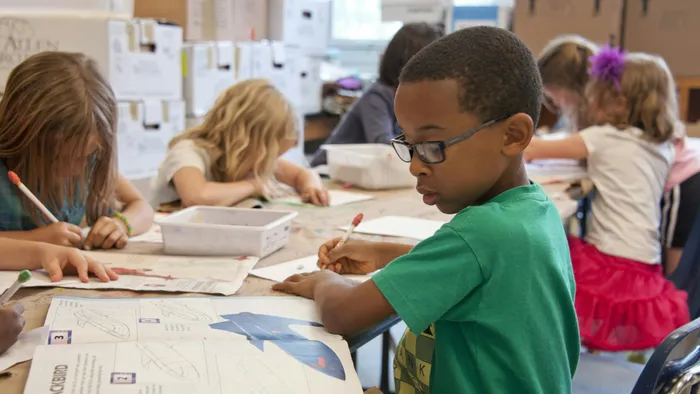 A group of children drawing in the classroom, with one child at the forefront, wearing a green shirt.