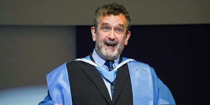 A university professor dressed in blue and black academic gown and speaking at a lecture.