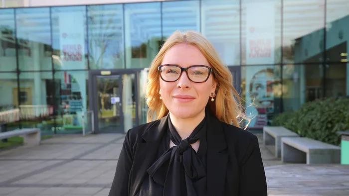 A blonde woman wearing black and glasses, smiling outside the Leeds Trinity University reception.