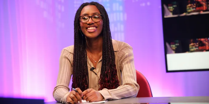 Female student sits at news desk smiling