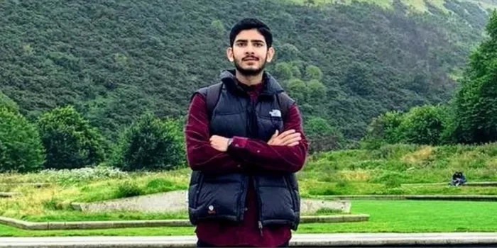 Asian male stands with arms folded in front of foliage background