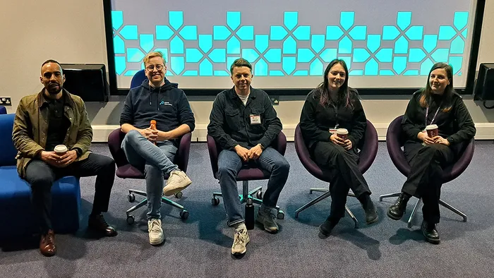 A panel of speakers sitting down in front of a colourful screen.
