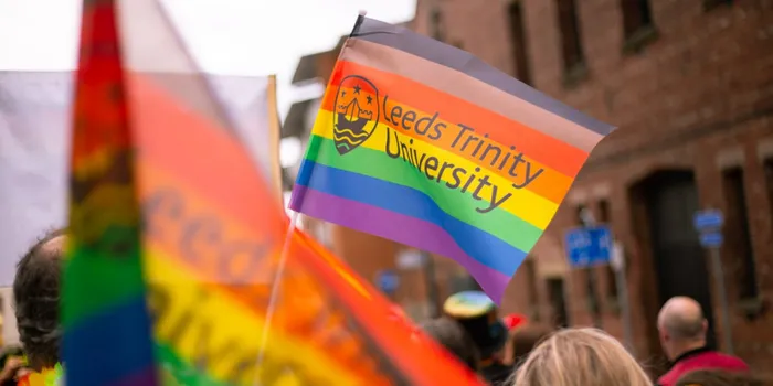 Rainbow flag with Leeds Trinity University logo is held in the air
