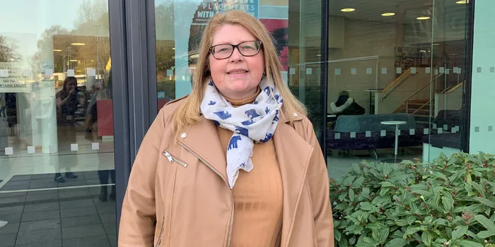 Female with light hair and glasses stands in front of glass building