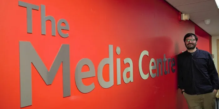 Male stands in front of red wall with The Media Centre in large writing on