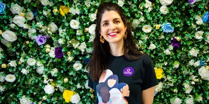 Female adult with brown hair stands in front of flower wall