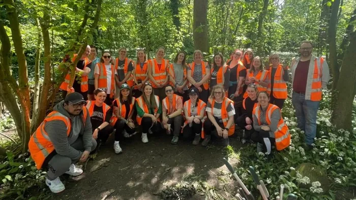 A large group of people wearing orange safety vests pose for a picture surrounded by trees