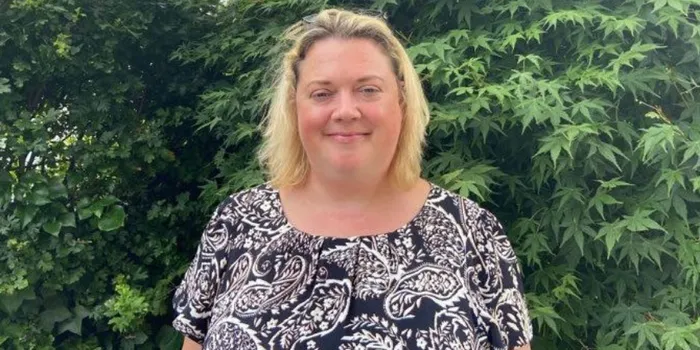 Blonde female with short hair stands in front of green bush