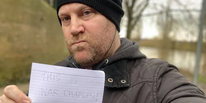 Man pictured in black hat, black coat and holding sign which reads 