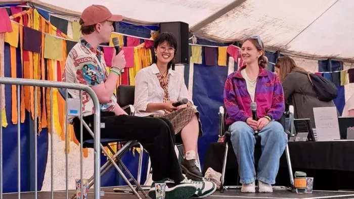 A student sits on stage with two music artists during an interview.