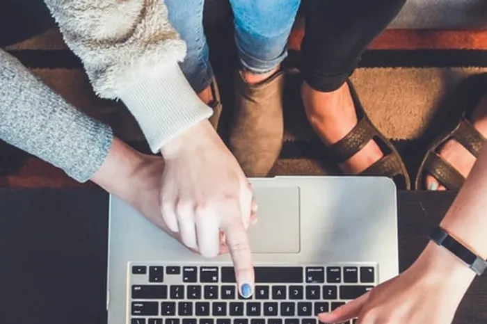 Three pairs of hands pointing to laptop