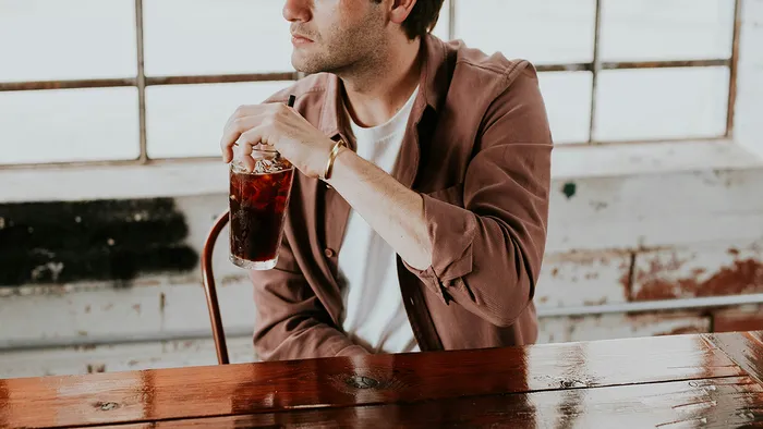 A man in a brown jacket holding a drink and turned towards the left side.