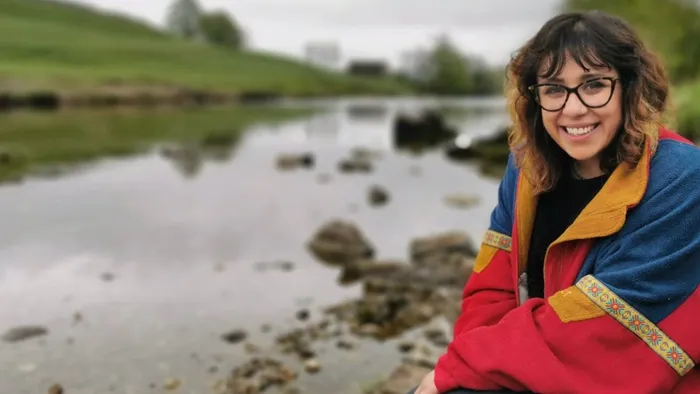 A woman wearing a red coat sits next to a body of water