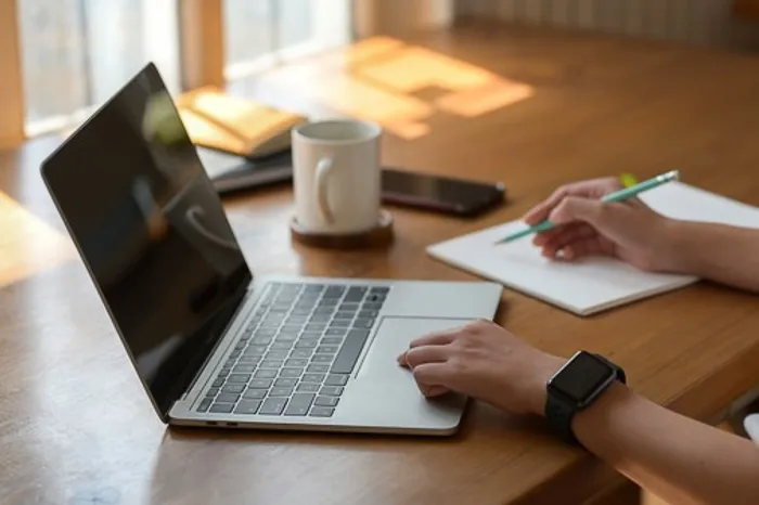 Student writing notes while using a laptop.