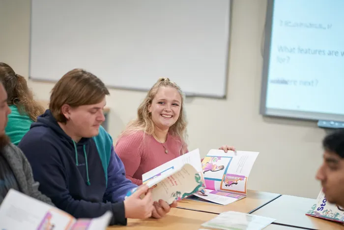 People sit at a classroom table holding colourful booklets