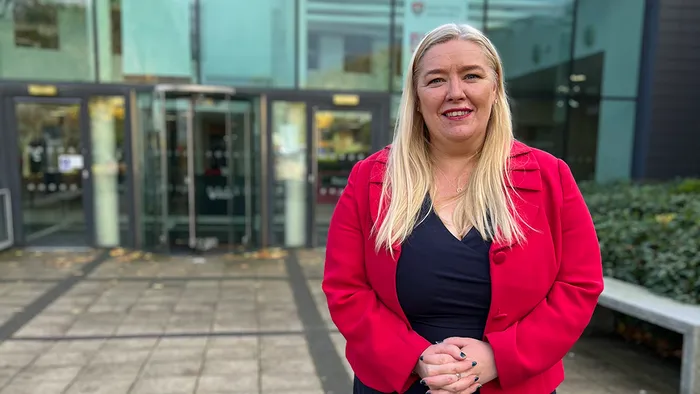 A female academic with long blonde hair and wearing a red jacket smiling.