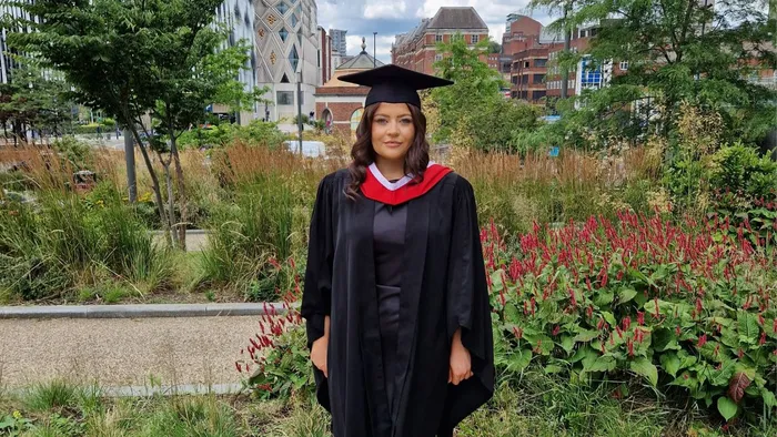 A girl with dark hair wearing a black cap and gown smiles for a picture