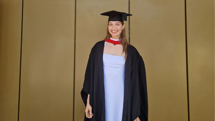 A girl wearing a black cap and gown over a white dress smile for a picture