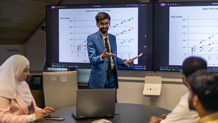 A man in a blue suit presenting a chart of sales during a business lecture.