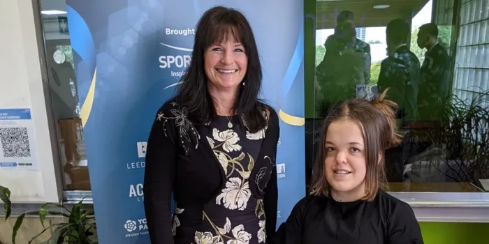 From left to right: brunette woman in floral dress and light brown woman in black dress with glass trophy