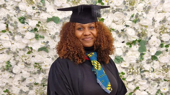 A graduate stand in front of a white flower wall