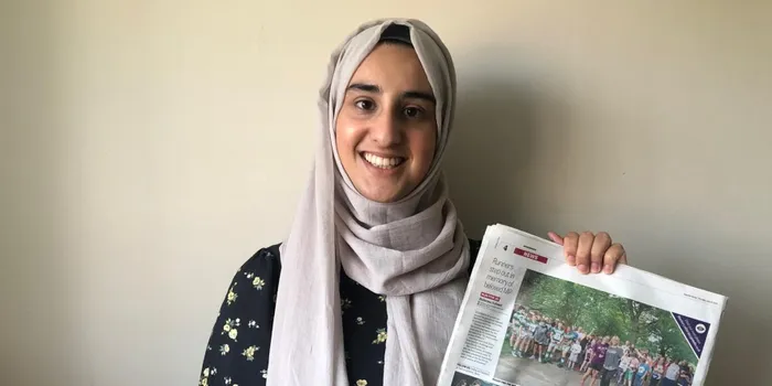 Female student in grey headscarf holding newspaper