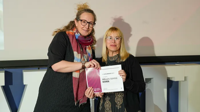 A mature student holding a Dean Award diploma that reads Helen Marie Khan on the right, and a female member of Executive on the left.