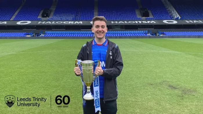 Leeds Trinity alumnus Howard Bloom holds a trophy while standing on a football pitch