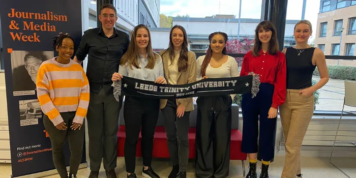Group of students line up in front of window holding Leeds Trinity University black scarf