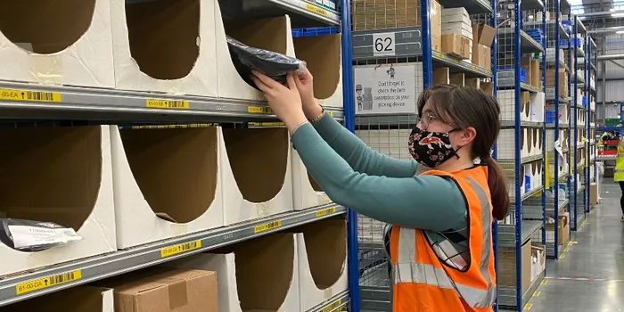 Student stacking shelves in orange hi-vis jacket
