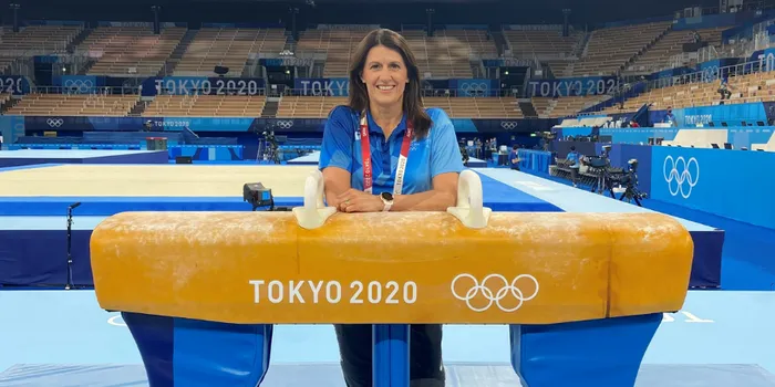 Woman with brown hair in tracksuit leans on pommel horse with Tokyo 2020 written on it