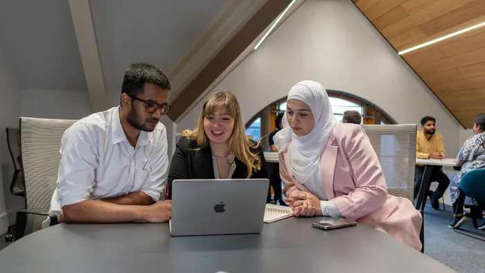 A group of three students looking at a computer in a modern study space at the Leeds Trinity University City Campus.