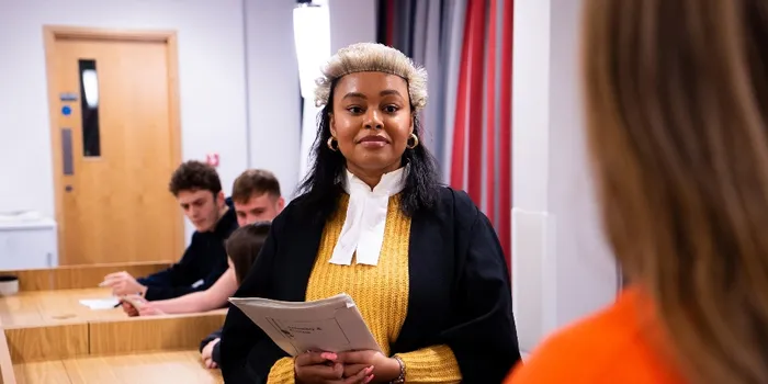 A student in solicitors court dress and yellow jumper, holding papers