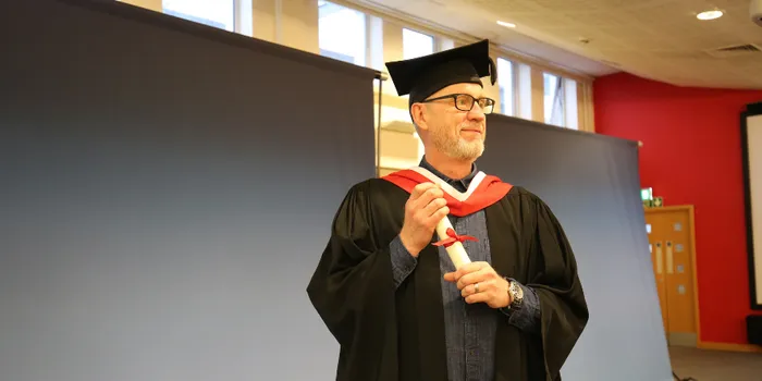 Mature male student in glasses and graduation cap poses for photo