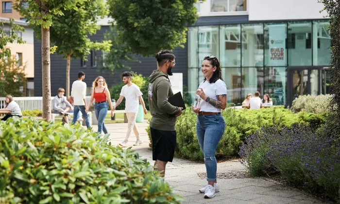 Two students outside on a green campus, in front of the Atrium