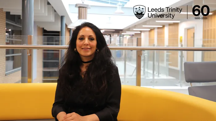 A female academic sitting on a yellow sofa and smiling. In the top right corner of the image, there is a black font logo reading Leeds Trinity University 60, 1966-2026.