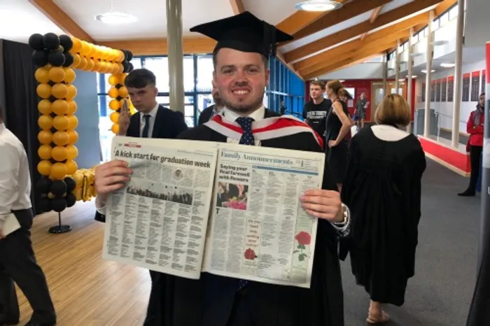 Tom pictured in cap and gown holding up newspaper